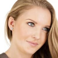 orhangen_nassmycke_titan_blomdahl_7330981560075_7330981157022_15-1491-01_17-1402-01.jpg صورة مقربة لامرأة شابة ذات عيون زرقاء وأقراط، تبرز ملامح وجهها ومجوهراتها. مثالية لسياقات الجمال والموضة.