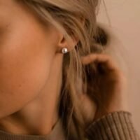 orhangen_titan_blomdahl_7330981154281_15-1233-59.jpg صورة مقربة لامرأة ترتدي أقراطًا أنيقة من اللؤلؤ، تعرض تصميمًا كلاسيكيًا للمجوهرات يعزز الجمال والرقي.