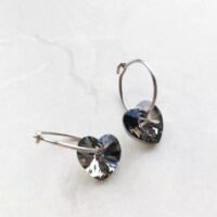 orhangen_titan_blomdahl_7330981158531_15-1255-12_b.jpg Heart-shaped crystal hoop earrings featuring a shiny silver finish and sparkling heart-shaped crystals, perfect for elegant accessories.