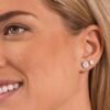 orhangen_titan_blomdahl_7330981560242_7330981521588_15-1465-01_15-12166-01.jpg Close-up of a woman wearing elegant diamond stud earrings featuring a round and a smaller stone, showcasing timeless jewelry design.