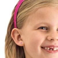 orhangen_nickelfri_plast_blomdahl_15-0114-42_7330981150214.jpg Young girl smiling with a pink headband and stud earrings, showcasing a cheerful expression and playful style.