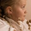 orhangen_nickelfri_plast_blomdahl_7330981150214_15-0114-42.jpg Profile view of a young girl wearing earrings, showcasing delicate jewelry against a soft background.