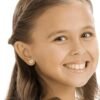 orhangen_nickelfri_plast_blomdahl_7330981510643_15-01121-01_a.jpg A young girl smiling while wearing heart-shaped earrings, showcasing a joyful expression and light brown hair.
