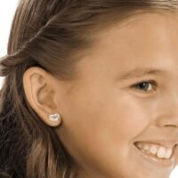 orhangen_nickelfri_plast_blomdahl_7330981510643_15-01121-01_b.jpg Heart-shaped diamond earrings worn by a smiling girl, showcasing a delicate and charming design suitable for children.
