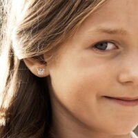 orhangen_nickelfri_plast_blomdahl_7330981512203_15-01125-01_b صورة مقربة لطفل ذو شعر طويل يرتدي أقراطًا فضية على شكل فراشة، مما يُظهر تصميم المجوهرات الدقيق والسحر الشبابي.