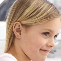 orhangen_nickelfri_plast_blomdahl_7330981512722_15-0114-98.jpg Close-up of a young girl with blonde hair wearing flower stud earrings, showcasing a delicate and stylish accessory for children.